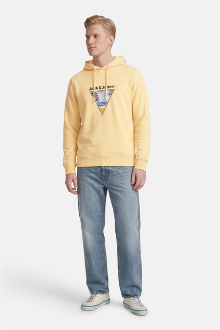 Pull à capuche jaune d'ORIGINALS BY JACK & JONES, avec un imprimé plage triangulaire sur la poitrine, combiné avec un jean bleu et des baskets blanches.