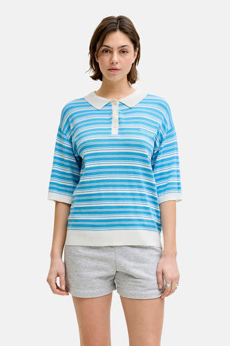 Pull rayé bleu de JJXX, avec un pull vert sur les épaules, un short gris et des chaussures marron.