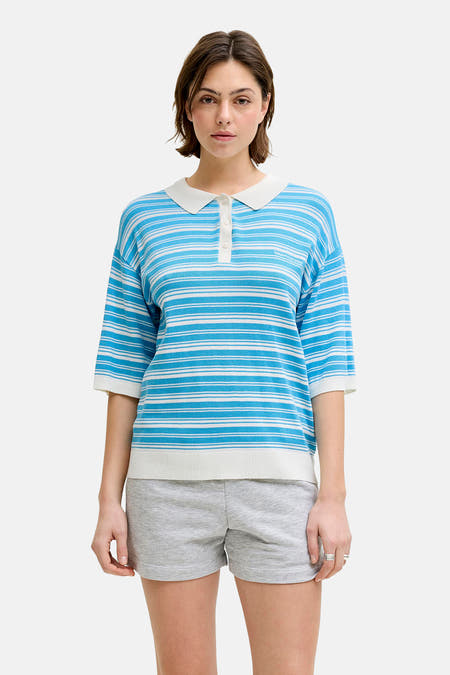 Pull rayé bleu de JJXX, avec un pull vert sur les épaules, un short gris et des chaussures marron.