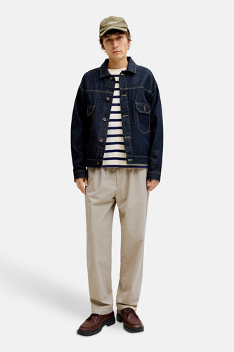 Man met pet, denim jack, gestreepte trui, beige broek en bruine schoenen.