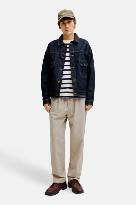 Man met pet, denim jack, gestreepte trui, beige broek en bruine schoenen.