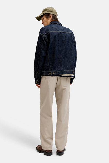 Man van achteren, draagt pet, denim jack, beige broek en bruine schoenen.