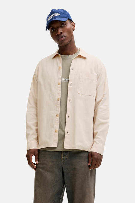 Beige overhemd met lange mouwen van ORIGINALS BY JACK & JONES, met knoopsluiting en borstzak, gedragen over een groen T-shirt en donkere jeans.