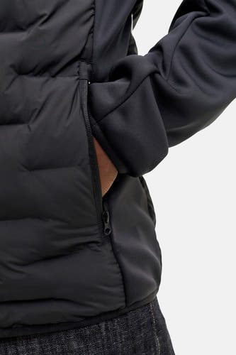 Manteau court noir de CORE BY JACK & JONES, avec poche à fermeture éclair et main visible dans la poche.