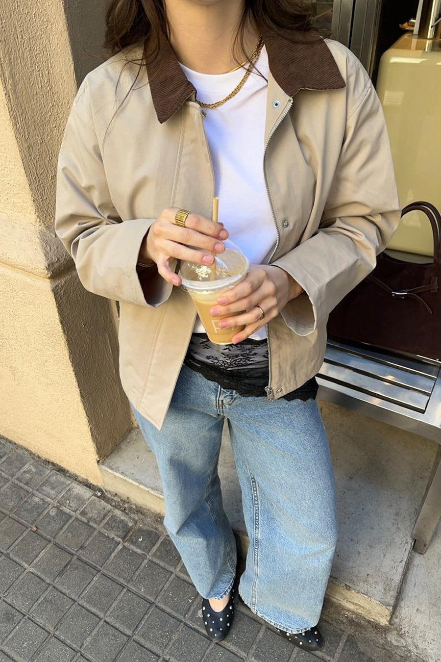 Manteau court beige de JJXX avec col côtelé marron, porté sur un t-shirt blanc et un jean, avec un café glacé à la main.