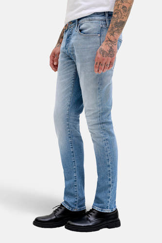 Jean slim de denim bleu clair de JACK & JONES JEANS INTELLIGENCE, avec des tatouages sur la main et des chaussures noires.