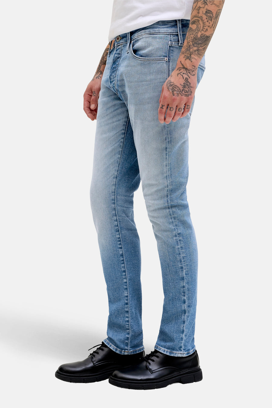Jean slim de denim bleu clair de JACK & JONES JEANS INTELLIGENCE, avec des tatouages sur la main et des chaussures noires.