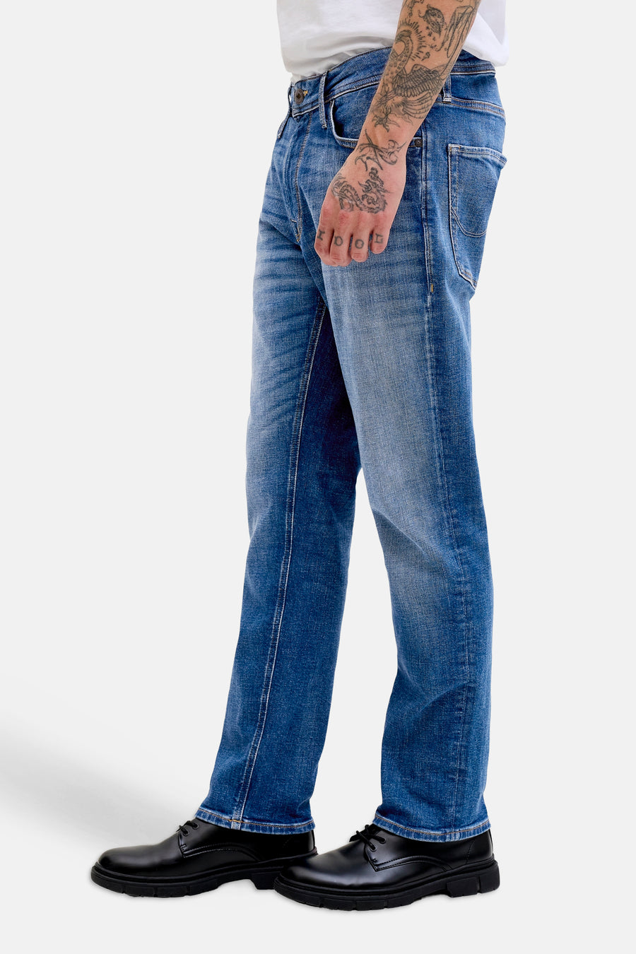 Jean droit bleu moyen de JACK & JONES JEANS INTELLIGENCE avec un aspect usé, associé à des chaussures noires et un bras tatoué.