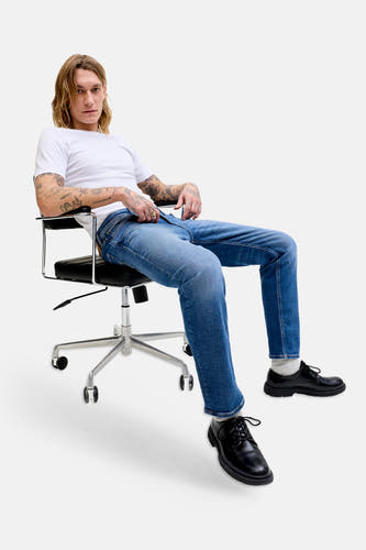 Jean droit bleu denim de JACK & JONES JEANS INTELLIGENCE, porté par un homme assis avec un T-shirt blanc et des chaussures noires.