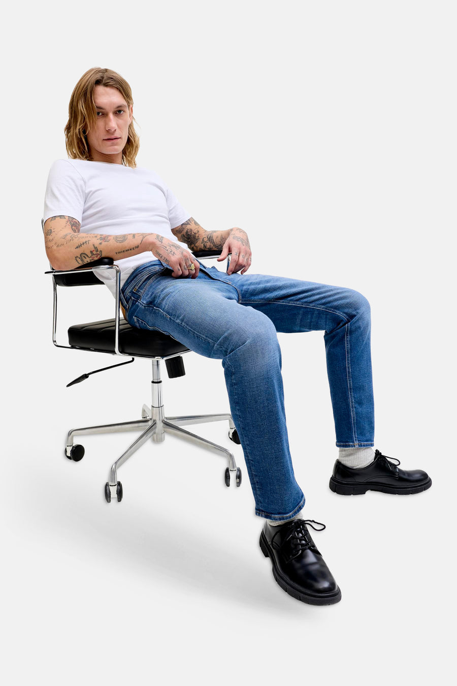 Jean droit bleu denim de JACK & JONES JEANS INTELLIGENCE, porté par un homme assis avec un T-shirt blanc et des chaussures noires.