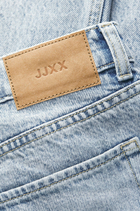 Close-up van een blauwe spijkerbroek met leren JJXX-label.

