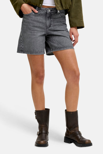 Short en jean gris foncé de JJXX, porté par un mannequin avec une veste vert olive, un haut blanc et des bottes marron.