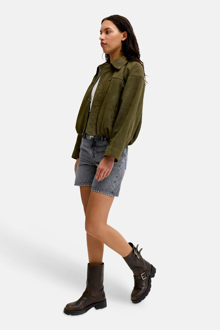 Short en jean gris foncé de JJXX, porté par un mannequin avec un blouson bomber vert olive et des bottes de motard marron.