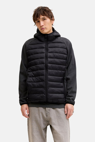 Staande man met zwarte gewatteerde jas en grijze jeans.
