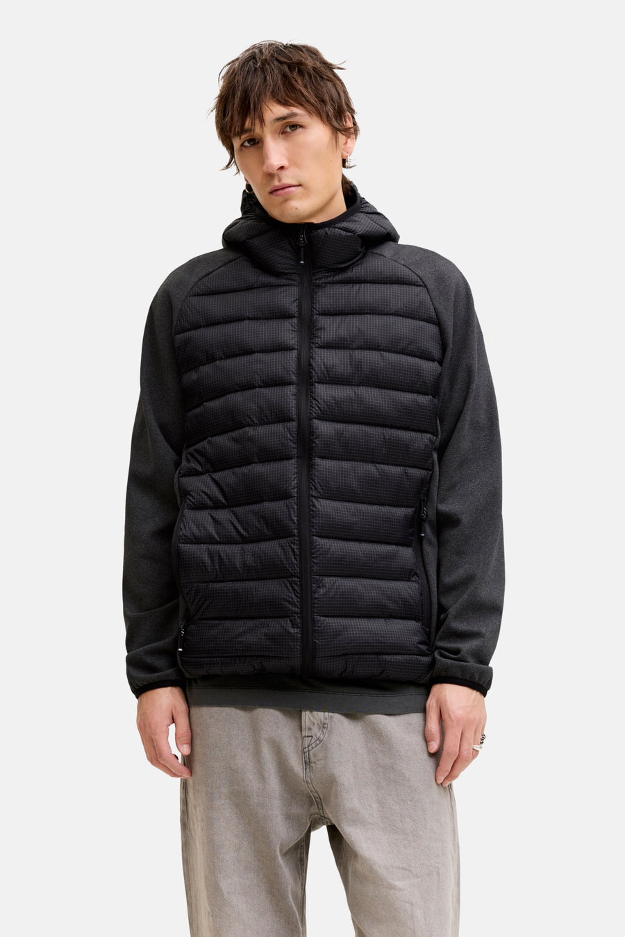 Staande man met zwarte gewatteerde jas en grijze jeans.
