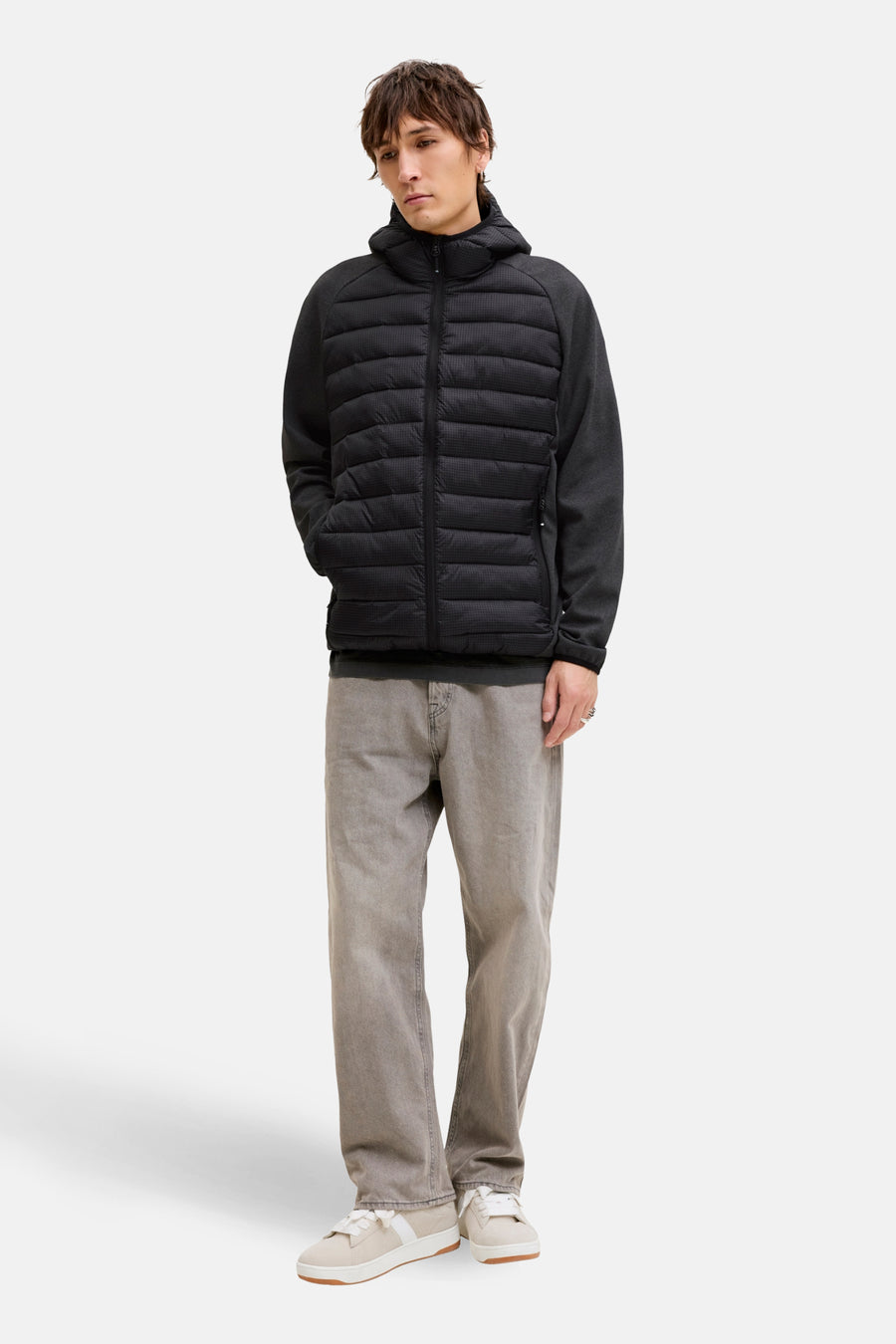 Man met zwarte gewatteerde jas, grijze broek en witte sneakers.
