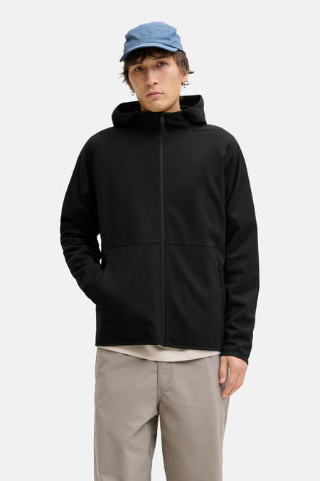 Gilet noir de CORE BY JACK & JONES, avec des manches longues et un capuchon, associé à une casquette bleue et à un pantalon gris.