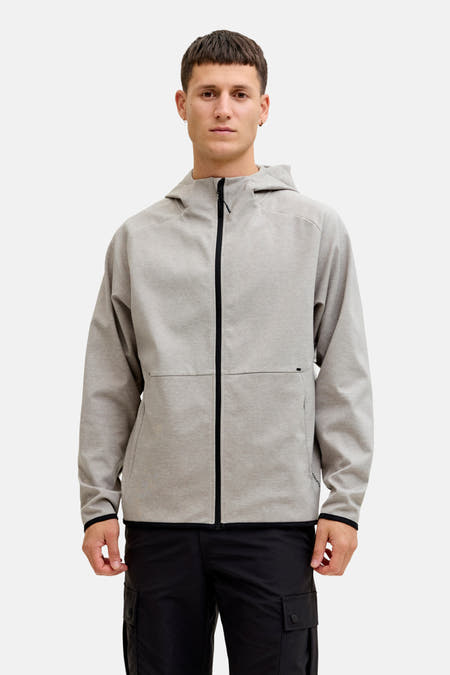Gilet gris de CORE BY JACK & JONES, avec des manches longues et une fermeture éclair, porté avec un pantalon noir et des baskets.