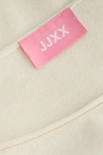 Pull de couleur écru de JJXX avec une structure en maille fine et une étiquette rose de la marque.