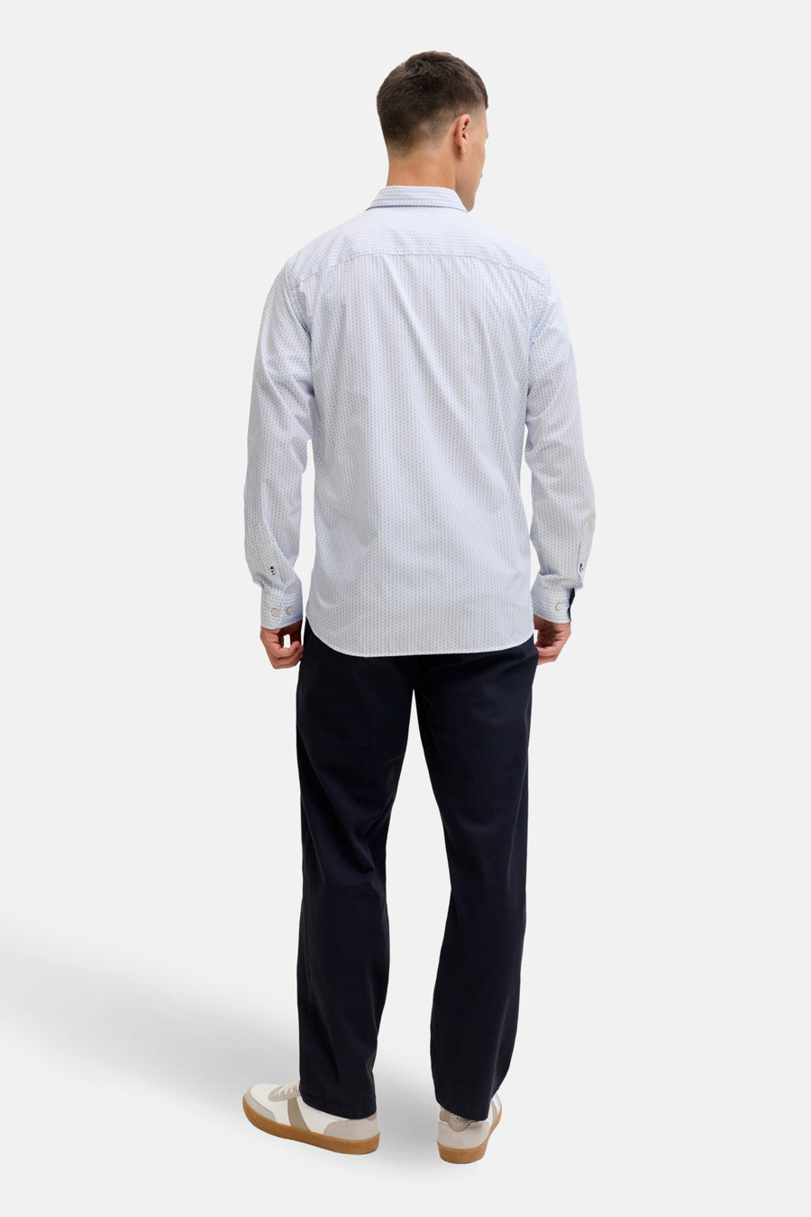 Man met overhemd, donkere broek en sneakers.