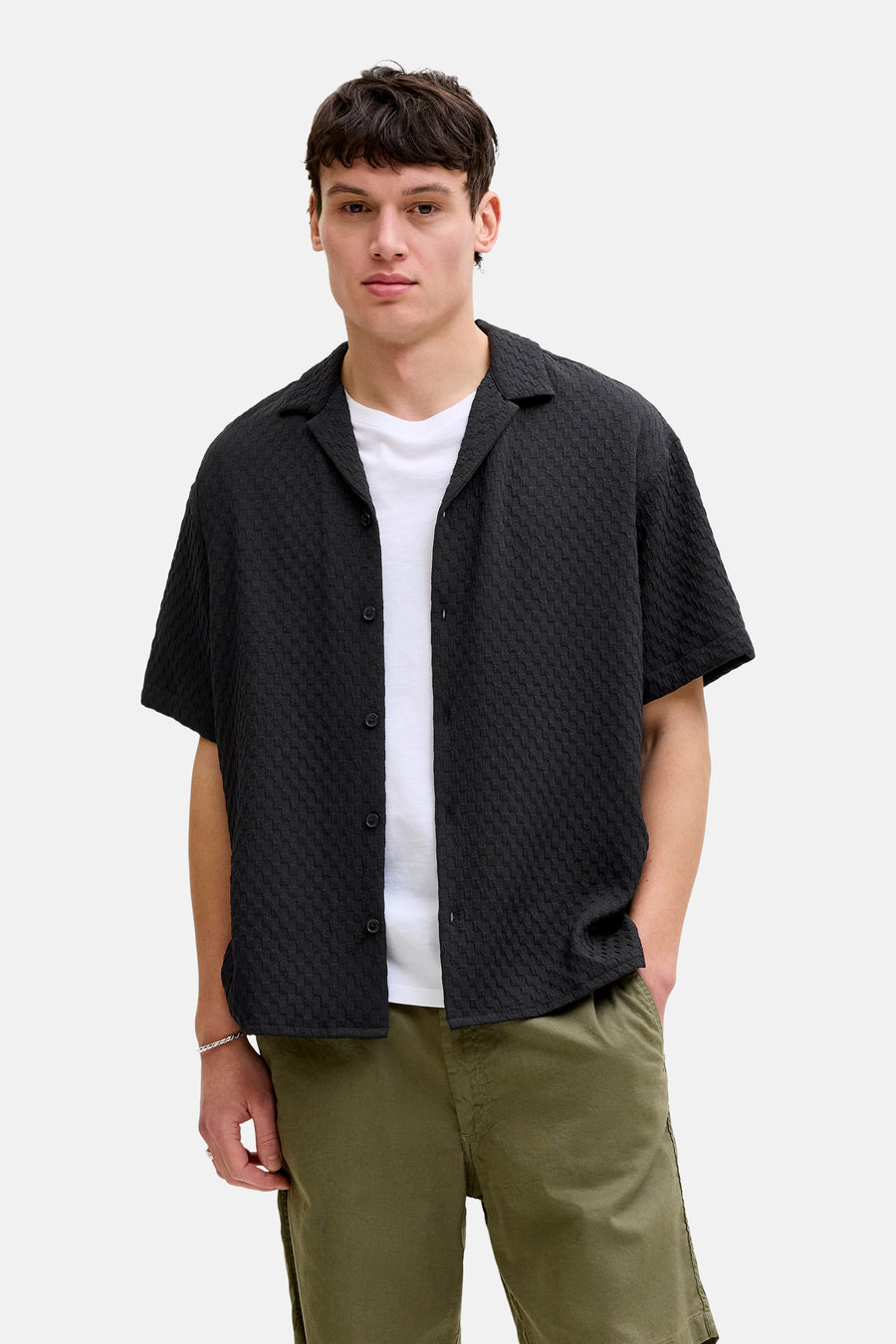Chemise noire à manches courtes de CORE BY JACK & JONES, avec une texture subtilement tissée, portée sur un t-shirt blanc et un pantalon vert.