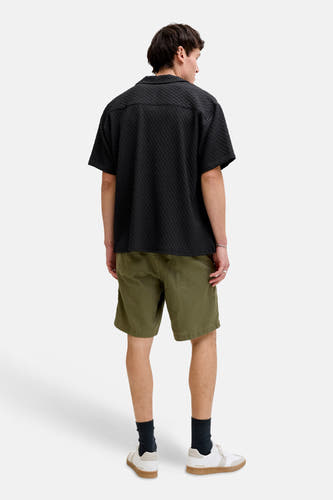 Chemise noire de CORE BY JACK & JONES, à manches courtes et à texture tissée, portée avec un short vert et des baskets blanches.