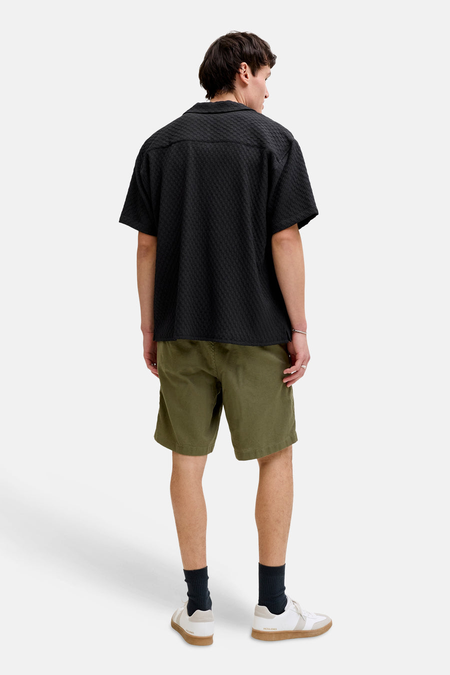 Chemise noire de CORE BY JACK & JONES, à manches courtes et à texture tissée, portée avec un short vert et des baskets blanches.