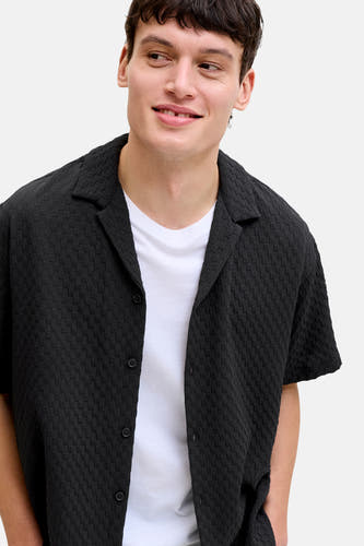 Chemise noire à manches courtes de CORE BY JACK & JONES, avec un motif subtil et portée sur un t-shirt blanc.