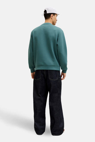 Pull bleu de CORE BY JACK & JONES, vu de dos, combiné avec un jean ample et une casquette blanche.
