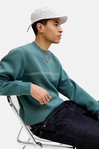 Sweat-shirt bleu de CORE BY JACK & JONES à manches longues et col rond, associé à une chaîne argentée et une casquette blanche.