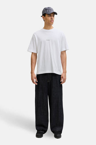 Wit T-shirt met korte mouwen van CORE BY JACK & JONES, gedragen met wijde donkere jeans en een pet met patroon.
