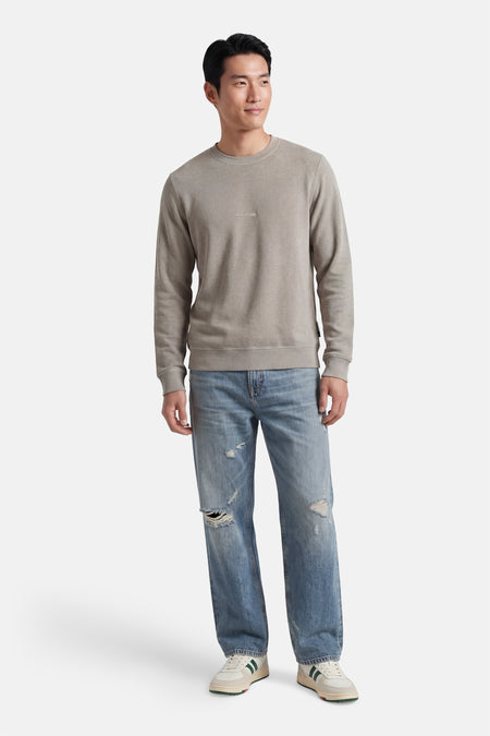 Pull gris de CORE BY JACK & JONES avec col rond, texture subtile et logo brodé, porté sur un jean déchiré et des baskets.