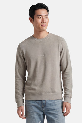 Pull gris à col rond de CORE BY JACK & JONES, avec une texture fine et un logo discret sur la poitrine, porté avec un jean clair.