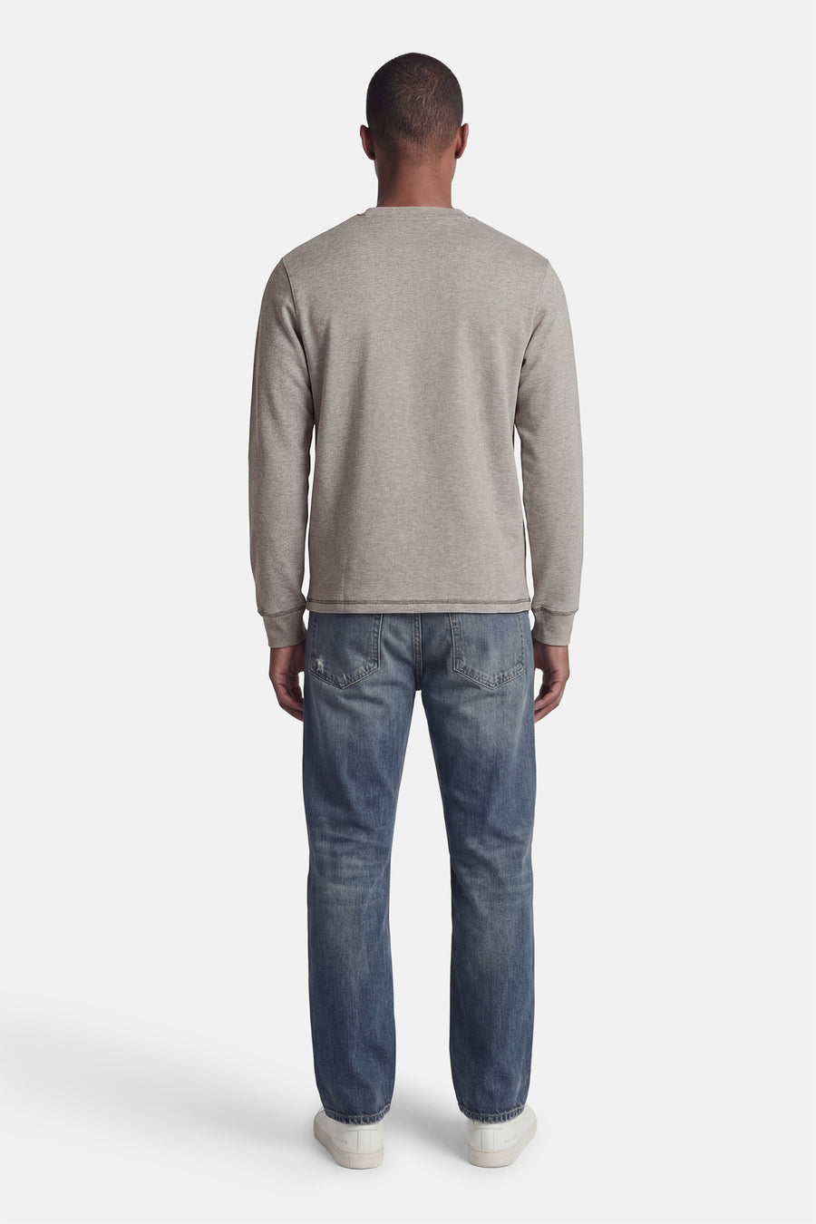 Pull gris de CORE BY JACK & JONES, à manches longues, col rond et poignets côtelés, porté de dos sur un jean bleu et des baskets blanches.