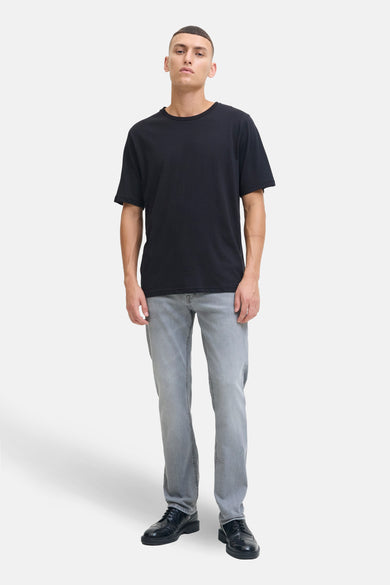 Jean slim fit gris clair de JACK & JONES JEANS INTELLIGENCE, associé à un T-shirt noir et des chaussures noires élégantes.