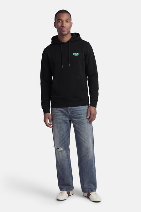 Sweat à capuche noir de CORE BY JACK & JONES, avec logo bleu sur la poitrine et combiné avec un jean déchiré et des baskets basses.
