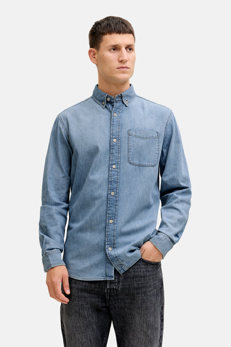 Man met denim overhemd en zwarte jeans, staand.

