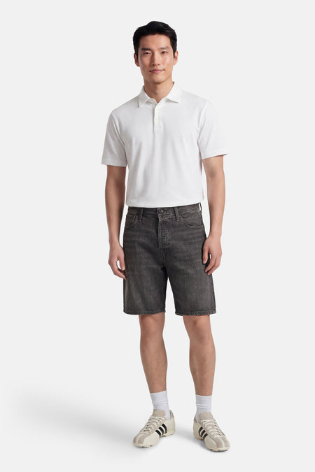 Grijze denim jeansshort van JACK & JONES JEANS INTELLIGENCE, gecombineerd met een wit poloshirt en crèmekleurige sneakers met zwarte strepen.