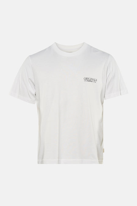 T-shirt blanc à manches courtes de ORIGINALS BY JACK & JONES, avec un petit logo sur la poitrine, porté avec un jean déchiré.