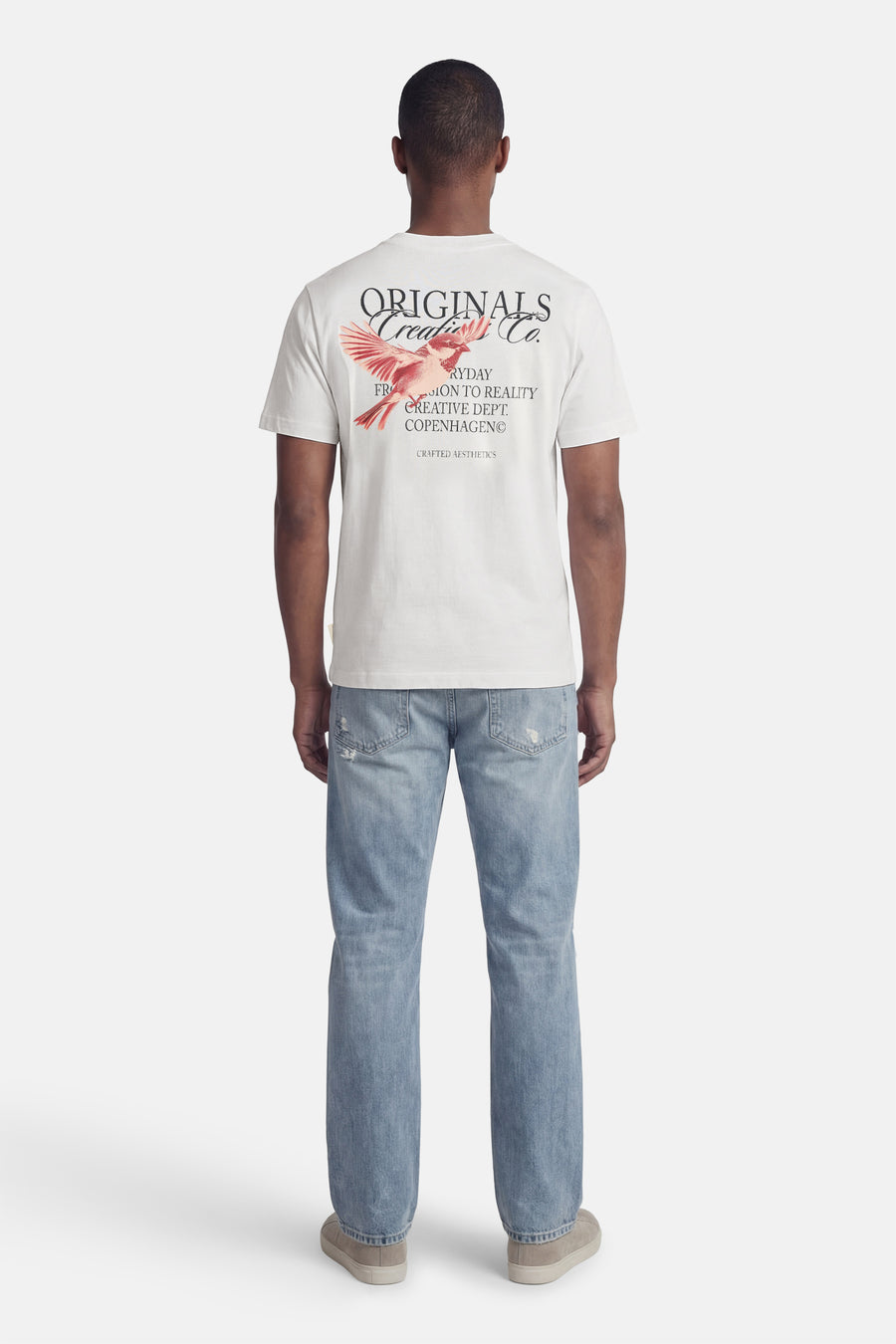 T-shirt blanc à manches courtes de ORIGINALS BY JACK & JONES, avec imprimé d'oiseau au dos, combiné avec un jean bleu et des chaussures en daim.