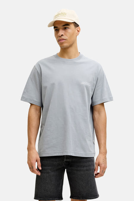 T-shirt bleu à manches courtes de ORIGINALS BY JACK & JONES, porté avec un short en jean noir et une casquette beige.