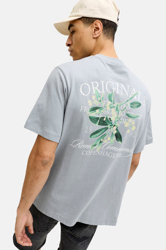 T-shirt bleu à manches courtes de ORIGINALS BY JACK & JONES, avec imprimé au dos et porté avec une casquette.