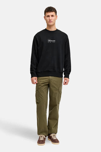 Pull noir de JJREBEL avec un logo sur la poitrine, combiné avec un pantalon kaki et des chaussures marron.