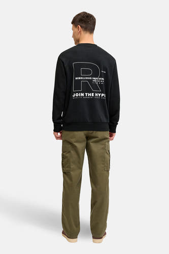 Pull noir JJREBEL avec imprimé graphique blanc dans le dos, combiné avec un pantalon cargo vert olive.