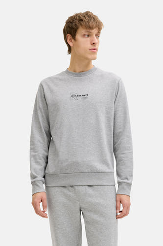 Pull gris à col rond de JJREBEL, avec un petit imprimé sur la poitrine, porté avec un jogging assorti et des baskets blanches.