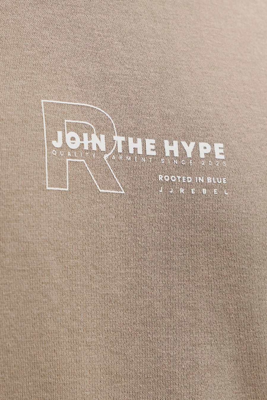 Pull marron de JJREBEL, avec texte blanc et logo sur la poitrine, sur un fond texturé.