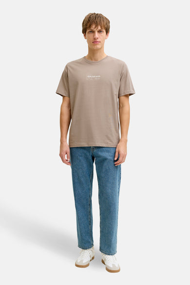 Bruin T-shirt met korte mouwen van JJREBEL, gedragen met jeans en witte sneakers.
