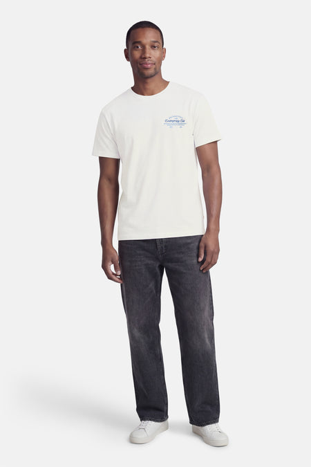 Wit T-shirt met korte mouwen van ORIGINALS BY JACK & JONES, met blauwe tekstprint op de borst, gedragen met donkergrijze jeans en witte sneakers.
