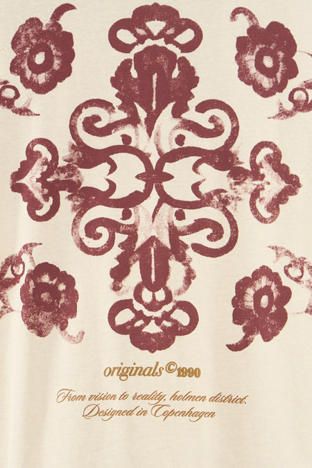 T-shirt beige de ORIGINALS BY JACK & JONES avec imprimé ornemental symétrique rouge foncé et texte doré 'originals © 1990' et 'Designed in Copenhagen'.