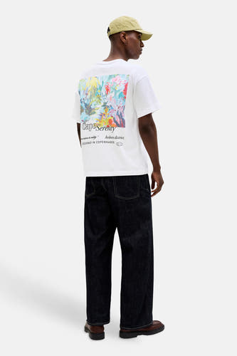 T-shirt blanc de ORIGINALS BY JACK & JONES, avec imprimé coloré et inscription au dos, combiné avec un jean foncé et des chaussures marron.